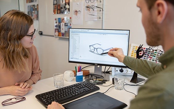 Zwei Personen an einem Schreibtisch, die einen 3D-Entwurf eines Brillengestells betrachten