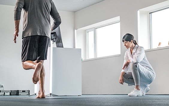 Healthcare professional crouching down to watch a patient running over a pressure plate