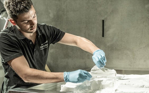 Man wearing gloves, removing 3D-printed insoles from a powder bed