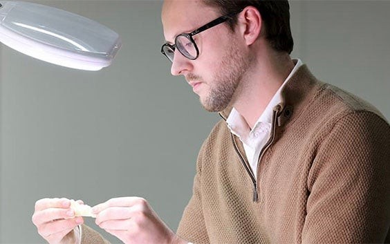 Mann betrachtet ein 3D-gedrucktes Teil unter einer Lampe