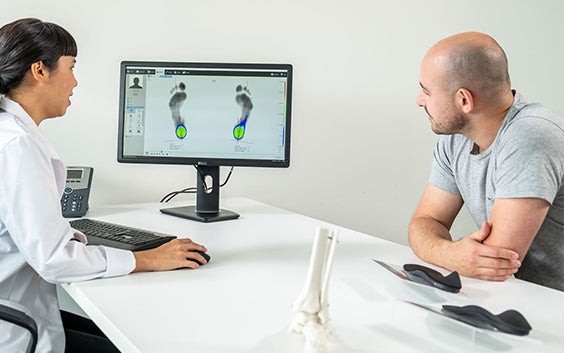A doctor and patient sitting at a desk, looking at digital measurements of feet