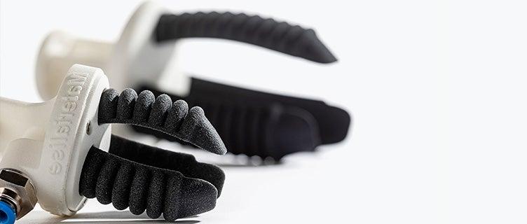 Two grippers with a rigid, round base and three flexible pneumatic fingers, shaped like bellows. The grippers are shown lying on their side and are not currently mounted on a robot.