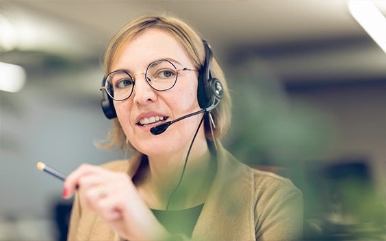 Customer support officer holding a pencil, talking while wearing a headset