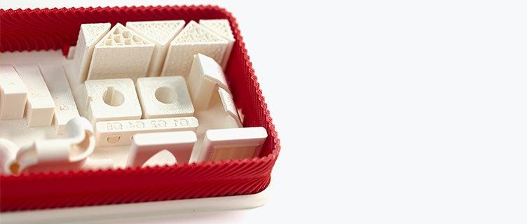 A series of white 3D-printed parts made from ABS-M30 using fused deposition modeling in a red box.