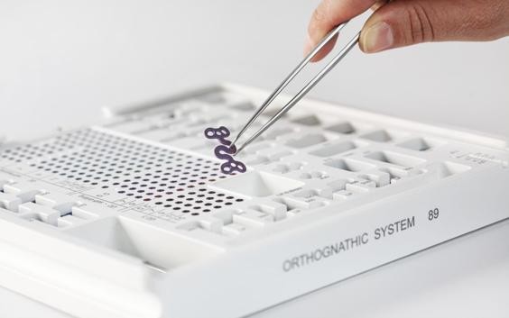 Hand picking up an S-plate from the orthognathic system set with tweezers