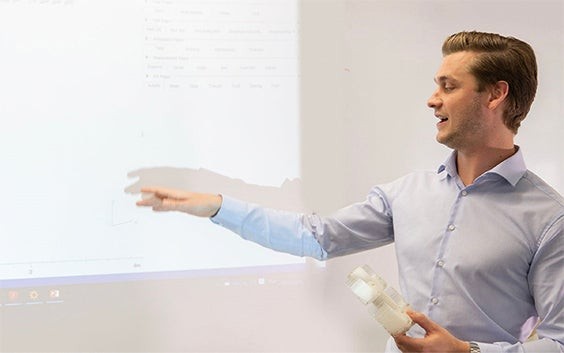 Man holding a 3D-printed part and pointing to a projector