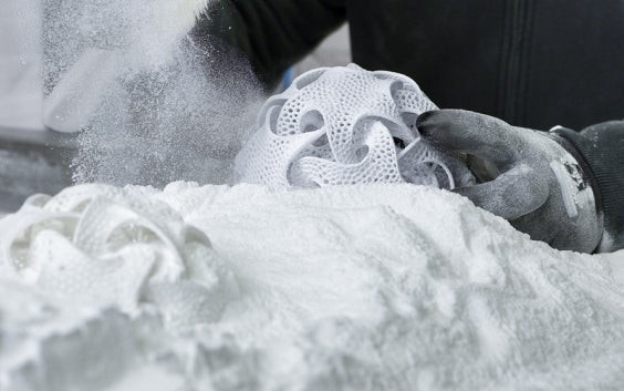 Gloved hands removing a ball-like 3D-printed part from 3D printing powder