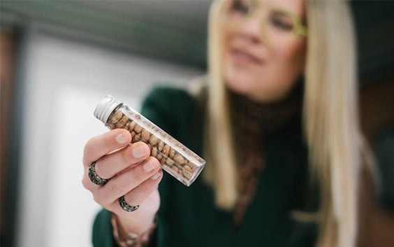 Une femme portant des lunettes imprimées en 3D brandit un récipient transparent rempli de graines de ricin.