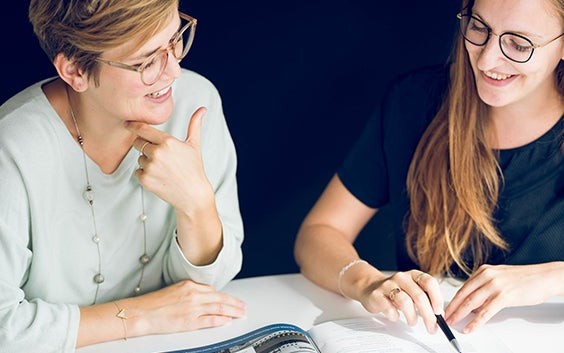 Two colleagues from Human Resources discussing a brochure during a meeting